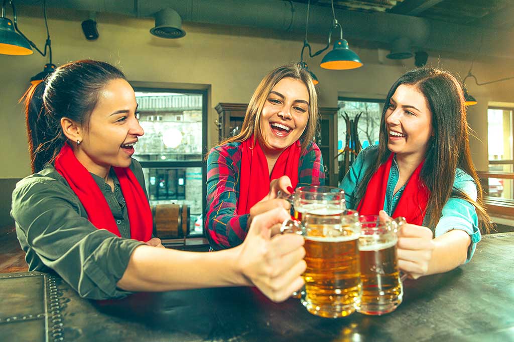 Sport, people, leisure, friendship, entertainment concept - happy female football fans or good young friends drinking beer, celebrating victory at bar or pub. Human positive emotions concept