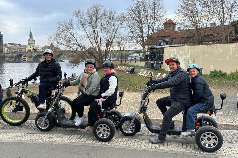 Familie mit Kindern auf Adventure Trikes an der Moldau mit der Karlsbrücke im Hintergrund